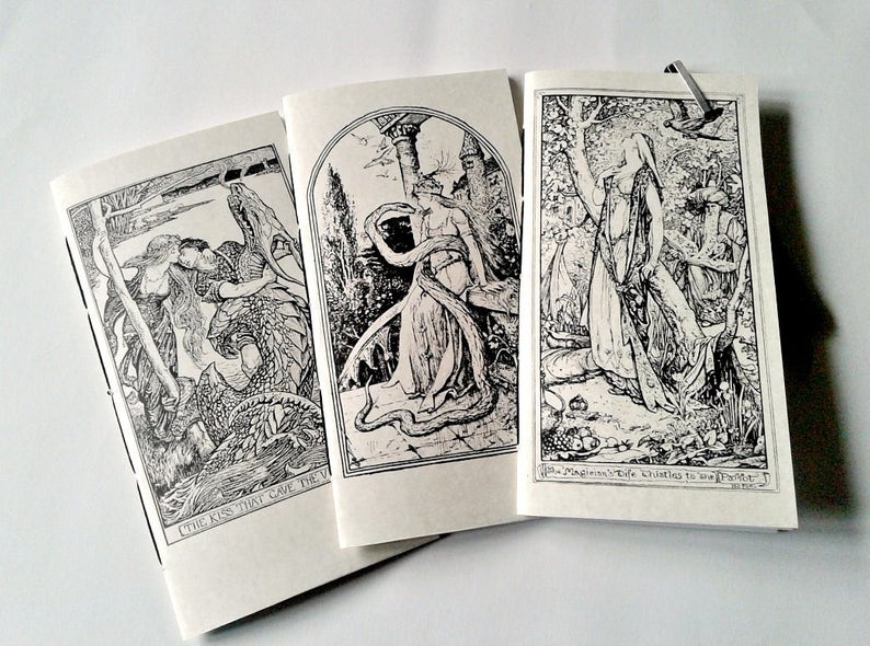 May include: Three off-white paper booklets featuring black ink illustrations. The left booklet shows a couple with a dragon, the centre shows a figure with a snake, and the right shows a person in a forest with the text The Magician's Wife Thistles to the Parrot.