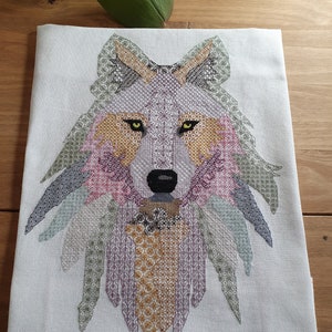 Könnte beinhalten: Eine Kreuzstich-Stickerei eines Wolfskopfes. Der Wolf besteht aus verschiedenen geometrischen Formen in verschiedenen Farben, darunter Grün, Lila, Pink und Orange. Die Augen des Wolfes sind gelb.