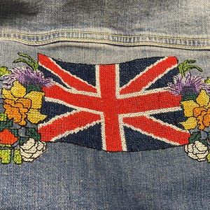 May include: A denim jacket with a cross-stitch design featuring a floral bouquet and a Union Jack flag.