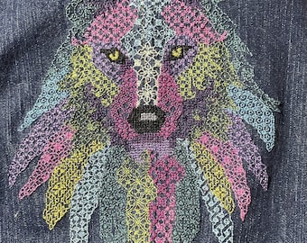 May include: A colorful embroidered wolf design on a dark blue denim fabric. The wolf's face is detailed with yellow eyes and a pink nose.