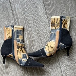 May include: A pair of ankle boots featuring a patchwork design of black suede, tan leather, and a blue and yellow tiger stripe pattern. The boots have a pointed toe, a side zipper closure, and a black kitten heel with a slim, tapered silhouette.