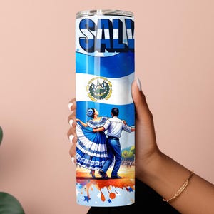 May include: A stainless steel tumbler with a colorful design featuring the flag of El Salvador, a couple dancing in traditional dress, and the word "SALVADOR" in large letters. The tumbler has a blue, white, and red color scheme.