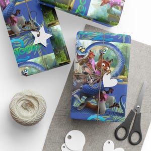 May include: Gift-wrapped presents featuring characters from the animated movie Zootopia. The wrapping paper is blue with images of the characters and a blue snake. The gifts are tied with twine and decorated with star and heart-shaped tags. A ball of twine, scissors, and tags are also visible.