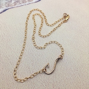 May include: A gold chain necklace with a gold fish hook pendant.
