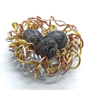 May include: A wire nest made of silver, gold, and copper wire with three fossilized stone eggs inside.