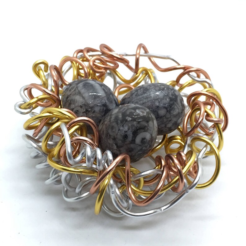 May include: A wire nest made of silver, gold, and copper wire with three fossilized stone eggs inside.