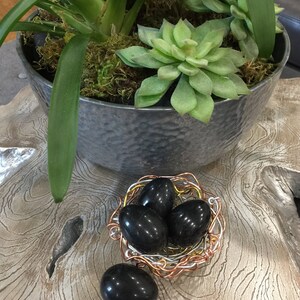 May include: Four black polished stones in a wire nest. The nest is made of copper and silver wire. The stones are smooth and round.