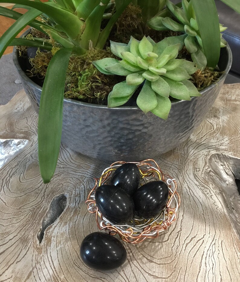 May include: Four black polished stones in a wire nest. The nest is made of copper and silver wire. The stones are smooth and round.