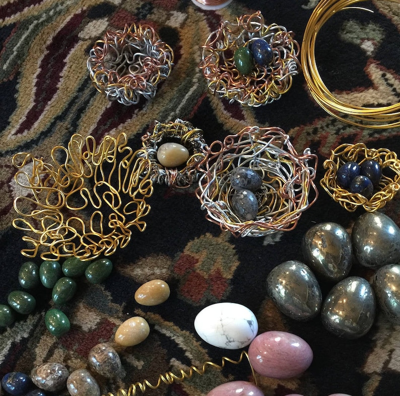 May include: A collection of wire nests, some with stones and others with small eggs, along with a variety of stones in different colors and shapes.