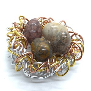 May include: A wire nest made of silver, copper, and gold wire with four colorful agate stones inside.