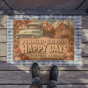 May include: A rectangular doormat with a gray and white plaid border featuring a vintage truck, pumpkins, and a barn. The text reads PUMPKINS HAYRIDES HAPPY DAYS PUMPKIN PATCH. The design includes a sign pointing to PUMPKINS HAYRIDES.