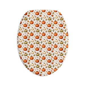 Op de afbeelding: Een ovale toiletbrilhoes met een herhalend patroon van oranje, witte en groene pompoenen, afgewisseld met bruine herfstbladeren en kleine takjes op een witte achtergrond, wat een dicht ontwerp met een oogstthema creëert.