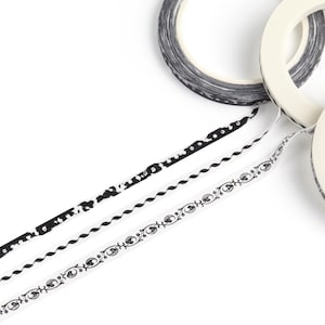 May include: An overhead shot features three rolls of decorative tape in black and white. Three strips of tape with different patterns extend from the rolls. The patterns include dots, wavy lines, and eye-like shapes. The background is white.