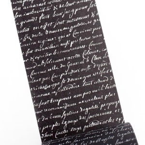 May include: A black and white patterned washi tape with a white background and black script text. The tape is rolled up and the end is visible.