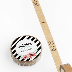 May include: A roll of brown washi tape with black numbers printed on it. The tape is partially unrolled and the roll is labeled "wintertime crafts washi tape" with a black and white striped background and a floral design.