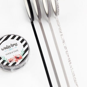 May include: Four rolls of washi tape. One roll has a black and white striped pattern with the text "wintertime" and "washi tape". The other three rolls are unrolled, showing a black tape, a gray tape, and a patterned gray tape with a floral design.