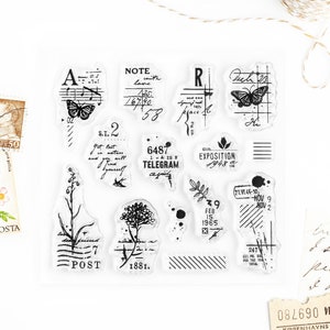 May include: Clear stamp set with various vintage-style designs. Includes butterflies, floral elements, musical notes, and text fragments like "NOTE," "TELEGRAM," and dates. The stamps are in black ink.