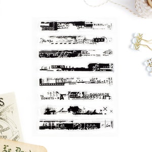 May include: A set of eight black and white vintage-style clear stamps with text and graphics. The stamps feature words like "Paris", "Cali USA", "Tomorrow", and "O.P.A.".