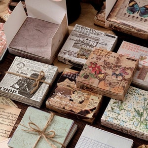 May include: Assortment of vintage-style decorative paper pads with floral, butterfly, and newspaper designs. The pads are packaged in boxes with a rustic aesthetic. The boxes have text in Japanese and English.
