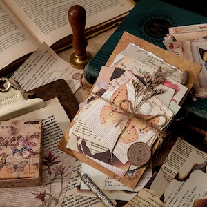 May include: A stack of vintage-style paper ephemera with butterfly and floral designs. The papers are tied with twine and have a wax seal. The papers are surrounded by other vintage-style papers and a book.