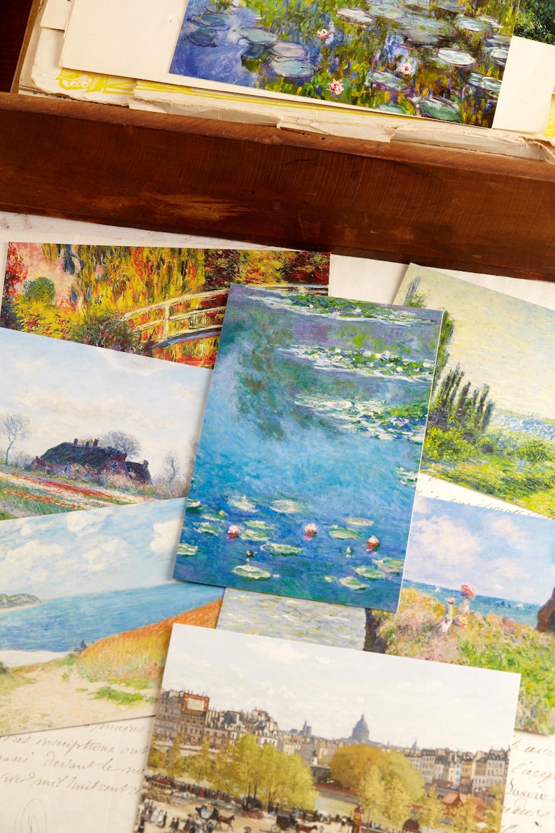 May include: A selection of art prints depicting impressionist paintings. The prints display scenes of water lilies, landscapes, and cityscapes, with a focus on vibrant colours and brushstrokes. The prints are displayed in a wooden box.