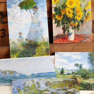 May include: A selection of art postcards displaying impressionist paintings. One card shows a woman with a green parasol, another a vase of sunflowers, and others depict landscapes with water lilies and sailing boats.
