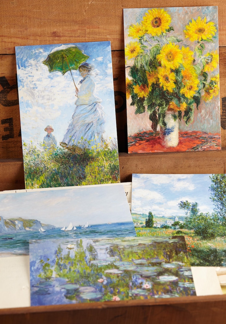 May include: A selection of art postcards displaying impressionist paintings. One card shows a woman with a green parasol, another a vase of sunflowers, and others depict landscapes with water lilies and sailing boats.