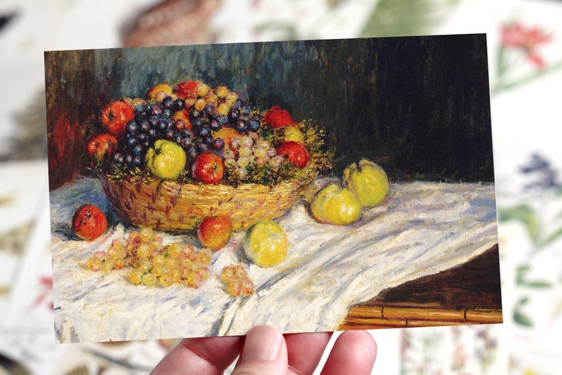 May include: A postcard depicting a still life painting of a basket of fruit. The basket contains red apples, purple and green grapes, and yellow quinces. The painting is on a white tablecloth.