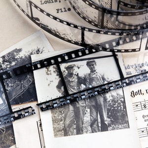 May include: A close-up of a vintage film reel, black and white photographs, and a sheet of music with German text. The film reel is partially unwound and the photographs are arranged on top of the music sheet. The text on the music sheet reads "Gott, wir loben dich".