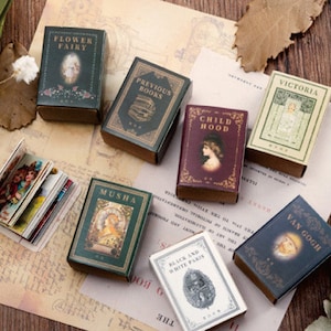 May include: A collection of miniature vintage book-shaped boxes with various designs and titles, including "Flower Fairy", "Previous Books", "Child Hood", "Musha", "Black and White Plains", "Victoria", and "Van Gogh".