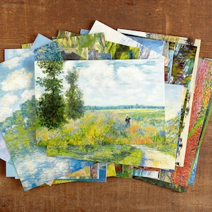 May include: A selection of art prints displaying impressionistic landscape paintings. The prints depict scenes with trees, fields, and skies in various colours, including blues, greens, and yellows. The prints are arranged on a wooden surface.