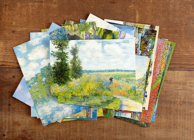 May include: A selection of art prints displaying impressionistic landscape paintings. The prints depict scenes with trees, fields, and skies in various colours, including blues, greens, and yellows. The prints are arranged on a wooden surface.