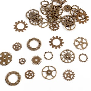 May include: A collection of bronze-colored metal gears of various sizes scattered on a white surface. The gears have different designs, including circular and star-shaped patterns, and are likely used for crafting or steampunk projects.