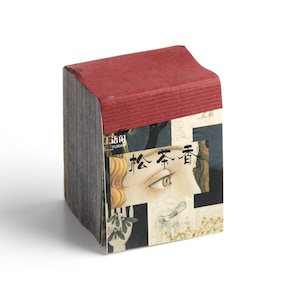 May include: A rectangular box with a red top and sides featuring a collage of images. The collage includes a partial image of a face with an eye and text in Japanese. The box is on a white background.