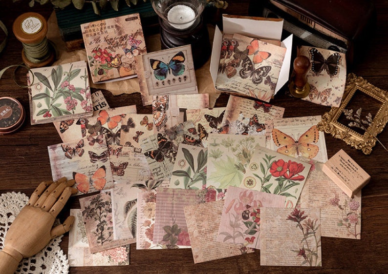 May include: A collection of vintage-style scrapbook paper featuring butterflies, floral designs, and other nature-inspired motifs. The paper is printed on a textured background and has a distressed look.