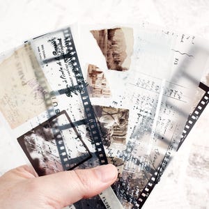 May include: A hand holds a collection of vintage-style ephemera. The assortment includes translucent film strips, aged paper with script, and torn paper with sepia-toned images. The overall aesthetic is a collage of nostalgic elements.