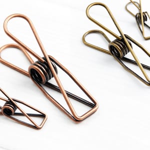 May include: Two metal clips in warm bronze and antique bronze finishes. The clips are made of wire and have a spring in the middle.