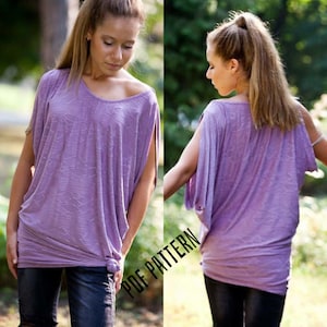 Puede incluir: Una blusa morada holgada de manga corta con un detalle anudado en la parte delantera. La blusa tiene un diseño ligeramente asimétrico con una manga cortada más alta que la otra. La modelo lleva la blusa con pantalones negros. El texto "PDF PATTERN" es visible en la imagen.