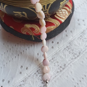 May include: A pink heart-shaped bead necklace with a silver clasp. The necklace is draped over a singing bowl and a red cushion.