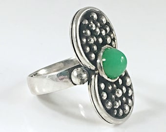 May include: A silver ring with a green gemstone set in a textured, oval-shaped design.