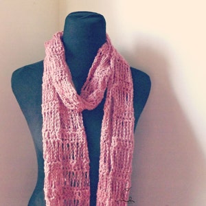 Könnte beinhalten: Ein rosa gestrickter Schal mit einem zarten Lochmuster. Der Schal ist über eine schwarze Schaufensterpuppe gelegt.