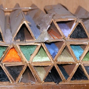 May include: A collection of glass rods in various colors are organized in triangular compartments. The rods are arranged in a pyramid shape, with the base of the pyramid being the widest part.