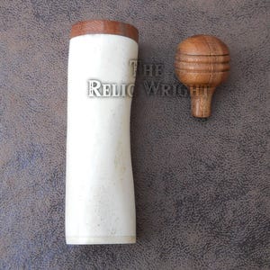 May include: A white and brown wooden container with a matching wooden stopper. The container is cylindrical with a slightly curved shape. The stopper is round with a small stem. The Relic Wright logo is visible.