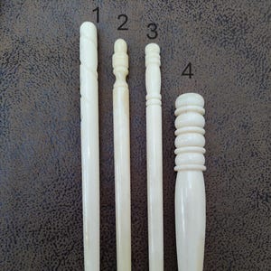 May include: Four ivory crochet hooks of varying sizes and styles. The hooks are numbered 1 through 4.