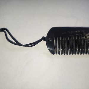 Könnte beinhalten: Ein schwarzer Kamm mit einem dunkelbraunen und weißen Muster, befestigt an einer schwarzen Schnur.