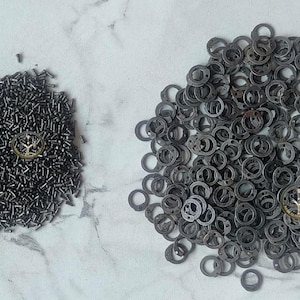 May include: Two piles of small metal pieces. One pile is made up of small, black, metal rods. The other pile is made up of small, black, metal rings.
