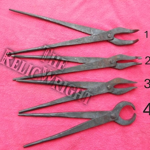 May include: Four hand-forged metal tongs of varying designs, laid out on a pink surface. The tongs have long handles and different shaped jaws, including pointed, flat, and curved styles. The metal has a dark, rustic finish.
