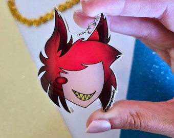 Könnte beinhalten: Ein klarer Acryl-Anhänger mit dem Gesicht einer Zeichentrickfigur mit roten Haaren, einem weißen Gesicht und gelben Zähnen. Der Anhänger ist an einem silbernen Schlüsselring befestigt. Der Anhänger hat den Text "@wingingitstudio".