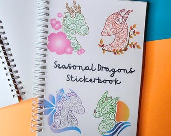 Może przedstawiać: Spiralnie oprawiony, biały zeszyt z naklejkami zatytułowany "Seasonal Dragons Stickerbook". Okładka przedstawia cztery kolorowe ilustracje smoków w kolorach zielonym, czerwonym, niebieskim i zielonym z różowymi, pomarańczowymi i niebieskimi akcentami.