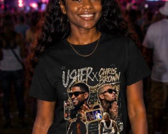May include: A black short-sleeve t-shirt featuring a graphic print of Usher and Chris Brown with the text Usher x Chris Brown. The shirt has a crew neckline and is paired with black leather-like pants, creating a dark, coordinated outfit.